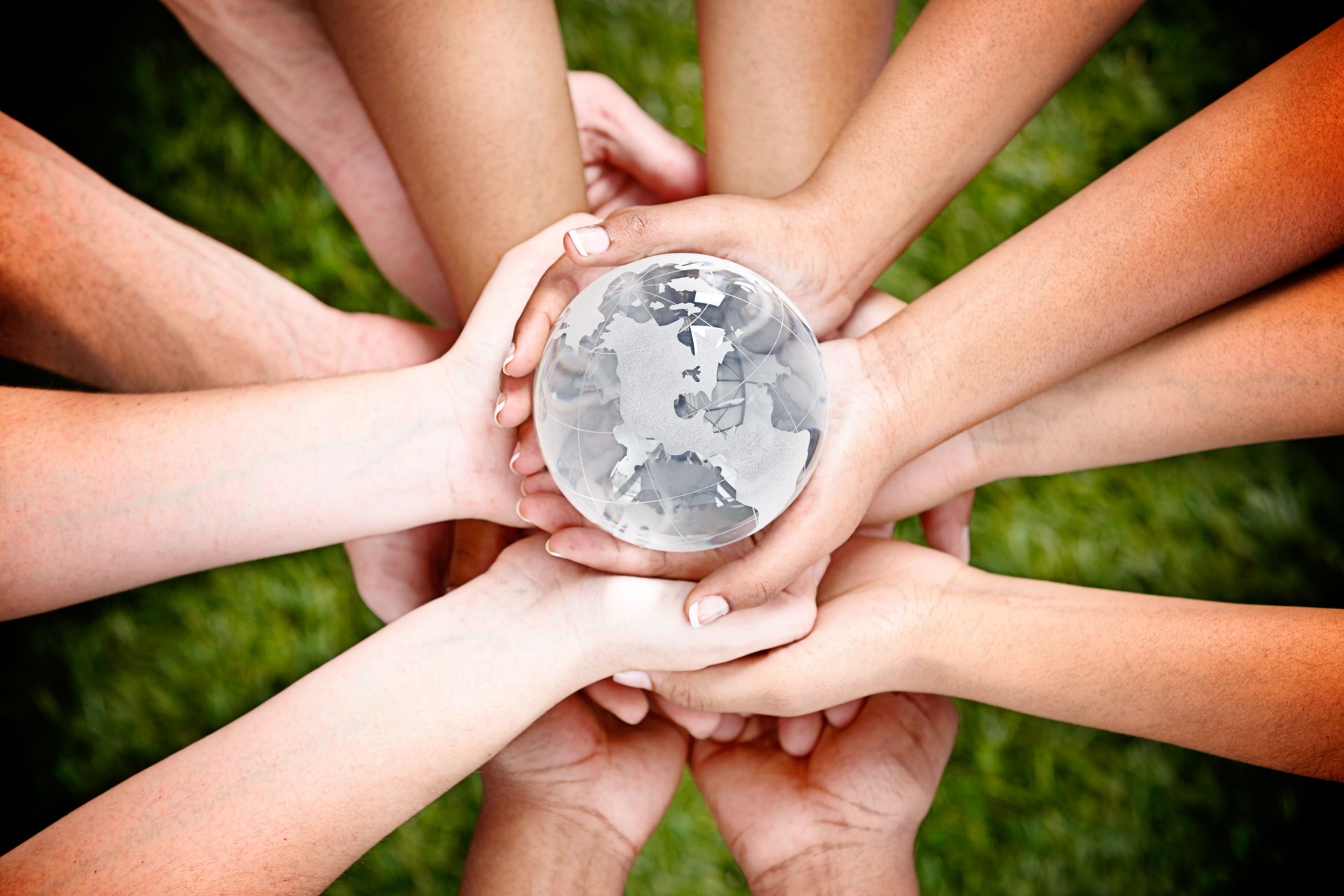 Many mixed hands cradle a crystal world globe carefully